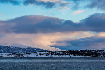 Northern Norway, winter cloudy landscape with fjords covered in snow. Scene near Tromso, colorful polar evening puffy clouds