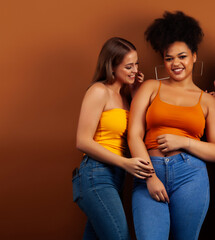 Fototapeta premium young pretty caucasian, afro woman posing cheerful together on brown background, lifestyle diverse nationality people concept