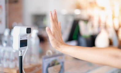 Female hand use digital temperature machine for measuring body temperature that placing a hand over the sensor in a cafe for mandatory checks of customers before come into the shop.