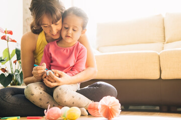 Fototapeta premium daughter sitting on her mother's legs decorating easter eggs