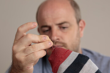 Close-up detail shot of a man sewing a sock by hand, with needle and thread. Selective focus on the sock. Emancipated man.