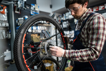 Fototapeta na wymiar Male mechanic working in bicycle repair shop, mechanic repairing bike using special tool, wearing protective gloves. Young attractive serviceman fixing customer's bicycle wheel at his own workshop