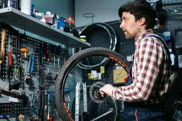 Young caucasian repairman repairing mountain bike wheel in bike shop workshop. Fixing bicycle. Caring for you wheels. man mechanic working in garage. Worker fixing cycle gear. Small business theme