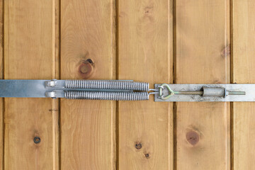 A device for tightening wood boards when drying out. Metal springs, adjustment nut with hinge. Wall of vertical planks. Concept of eliminating gaps in the wood with a clamp.