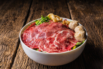 bowl of Thai style beef noodle with fresh sliced beef and fresh sliced ox shank and meatball and stewed beef on wooden table