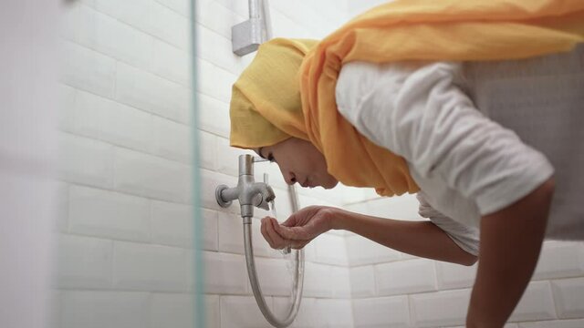 portrait of young Muslim woman perform ablution wudhu before prayer at home