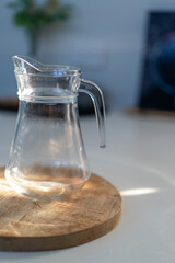 Glass water bottle jar with water glasses inside house lit by natural light from window on kitchen bench