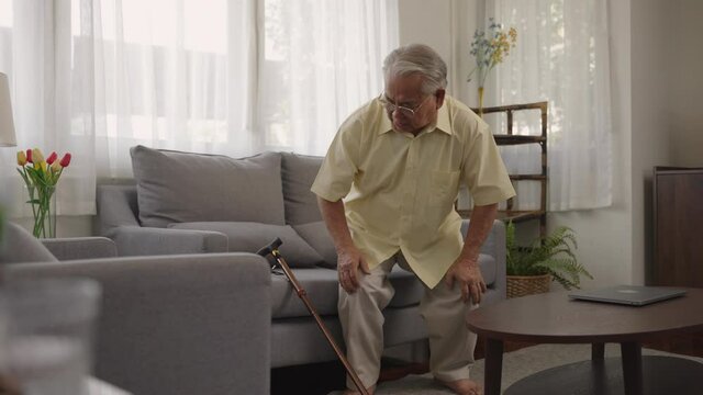 Asian old man hold wooden walking stick sit on couch in living room alone look at distance feels upset and lonely. Senior man alone in living room at home, senile diseases, healthcare concept