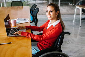 Young hispanic woman in wheelchair working with computer at workplace or office in Mexico city
