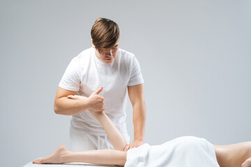 Side view of male masseur massaging lower part of leg to young unrecognizable woman in spa salon. Professional therapist men doing wellness massage shins and legs for female client.