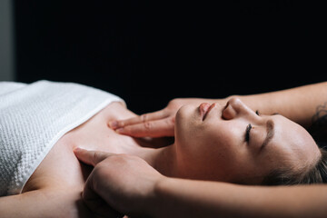 Fototapeta na wymiar Close-up side view of young woman lying down on massage table with closed eyes during shoulder and neck massage at spa salon. Male masseur professionally massaging shoulders on black background.