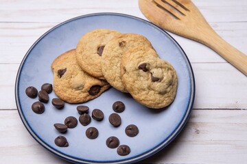 Close up of a plate of delicious chocolate chip cookies and scattered chocolate chips. Photographed in studio.