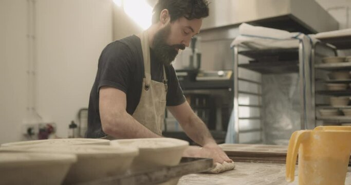 Male baker working in bakery kneading fresh dough on kitchen counter