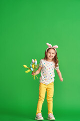 charming happy girl with Easter bunny ears and a bouquet of spring tulip flowers made of fabric on a green background in full growth. the child smiles and rejoices at the arrival of spring and Easter.