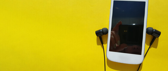 New concept of using the modern social app Clubhouse on a smartphone, headphones and smartphone on a yellow background, copy of the space, banner