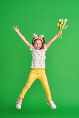 charming happy girl with Easter bunny ears jumps on a green background in full growth. a child...