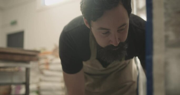 Male baker working in bakery putting fresh dough in push cart