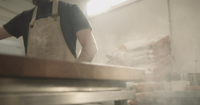 Male baker working in bakery putting flour on kitchen counter in sunshine