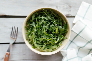 Green arugula salad leaves in bowl on wooden background. Healthy eating concept