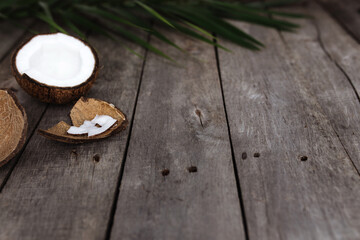 Broken coconuts on gray wooden background with palm leaf. White coconut pulp