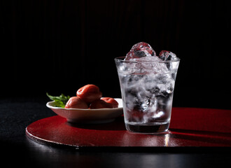 Shochu and pickled plums on a red tray against a black background with copy space.