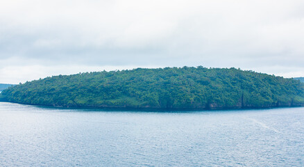 Coastal thickly wooded limestone landscape on cloudy day with smooth sea,New Caledonia.