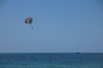 Fototapeta na wymiar Two people parasailing above blue ocean waters with a boat on the horizon on a sunny summer day with blue skies above.