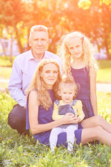 Fototapeta premium Parents with two little daughters at park. Happy family portrait. Nature lifestyle. Summer time. Caucasian people together. Outdoor parenthood