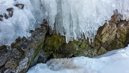 Early spring. The icicles on the rocks begin to melt. There is loose melted snow on the ground. Close-up. Stone texture.