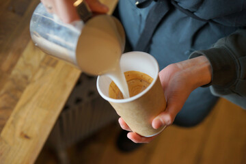 Barista prepares cappuccino in a paper cup
