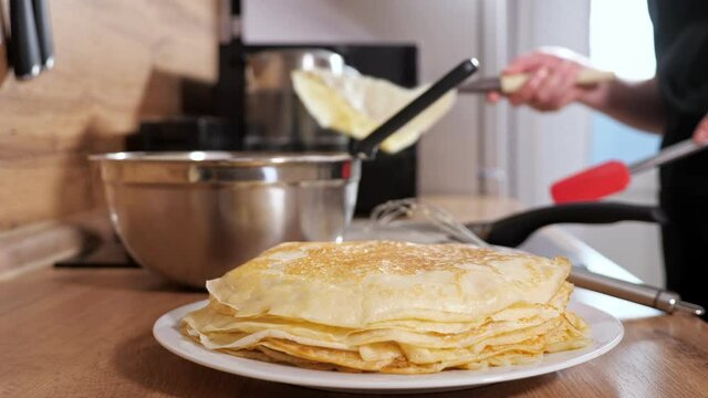 Unrecognizable woman puts a ready-made pancake with a spatula in a stack, slow motion.