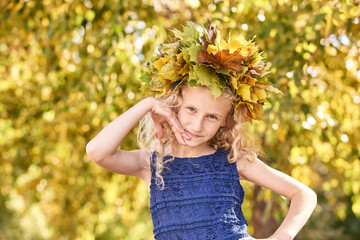 Little girl with autumn maple wreath. Yellow and green colors. Backyard nature. Female child portrait. Happy people. Model posing at park