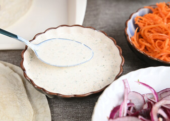 Liquid white sauce in a deep plate for making shawarma. A tablespoon scoops up the sauce.