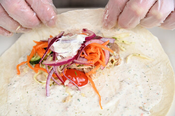 A vegetable mixture of carrots, cabbage, tomatoes and cucumbers, along with chopped fried chicken, lie on pita bread.