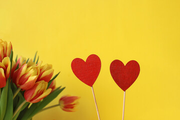 Fototapeta na wymiar two wooden red heart and tulips on yellow background