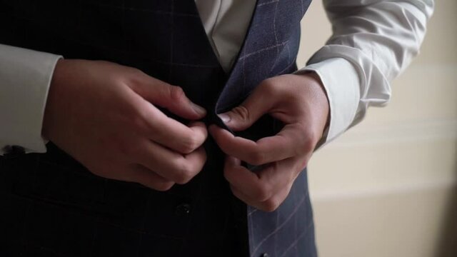 A young man buttons up his tuxedo jacket. Groom dresses for an event or wedding. High quality FullHD footage