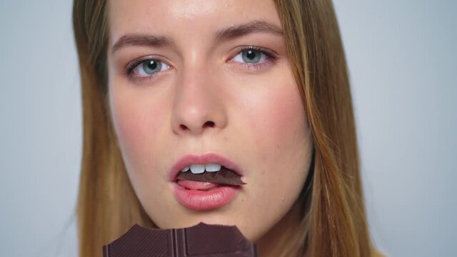 Closeup sensual woman enjoying chocolate at camera on grey background. - Powered by Adobe