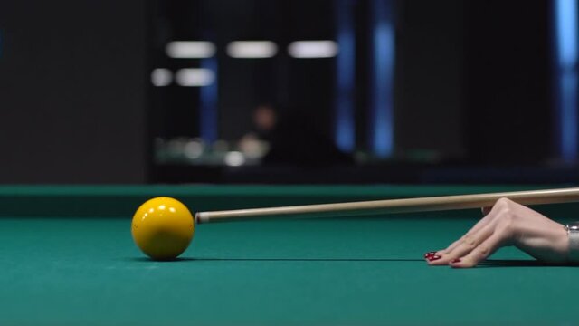 A woman's hand striking the cue ball on a billiards table, aiming at the yellow ball