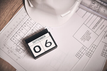 Labor Day 2021 concept. Workplace of engineer with drawings, white hardhat and calendar showing September 6 date. Helmet and blueprints at engineer workplace