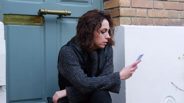 Caucasian young woman with blue eyes looking at her smartphone and waiting alone on a doorstep in Paris, France