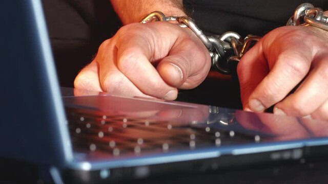 Conceptual shot of online freedom of speech restrictions. Handcuffed man&rsquo;s hands at laptop keyboard. Static shot.