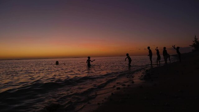 Children playing ricochet on the beach at sunset. Lagoon on Reunion Island.
