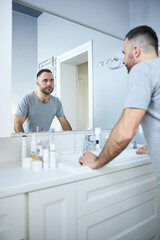 Bearded young man looking in the mirror in bathroom