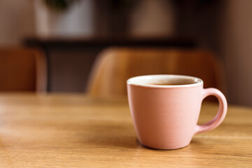 A pink ceramic cup of hot black coffee on a wooden table, cafe, copy space