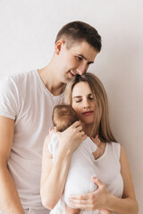 Woman and man holding a newborn. Mom, dad and baby. Close-up. Portrait of young smiling family with newborn on the hands. Happy family on a background.