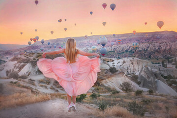 A girl with long hair and in a long dress at sunrise against the background of balloons in Cappadocia