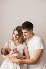 Woman and man holding a newborn. Mom, dad and baby. Close-up. Portrait of young smiling family with newborn on the hands. Happy family on a background.