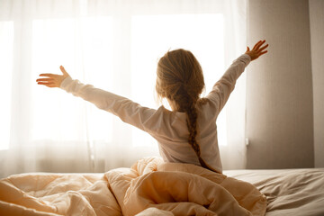 The girl woke up in the morning, sits on the bed, stretches and looks out the window, good morning...