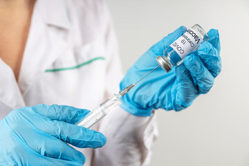 Vial withCOVID-19 vaccine and a syringe with a needle for injections for coronavirus infection in the hand of a doctor in a nitrile glove on a white background. Close-up. Concept fighting Coronavirus