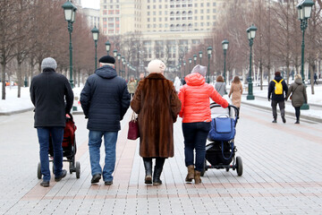 Family with baby prams walking on a spring city street in Moscow on crowd of people background
